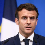 Man speaking at press conference with flags behind