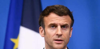 Man speaking at press conference with flags behind