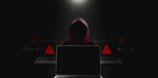 Hooded figure behind laptop cyber threat concept