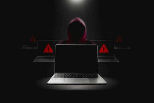 Hooded figure behind laptop cyber threat concept