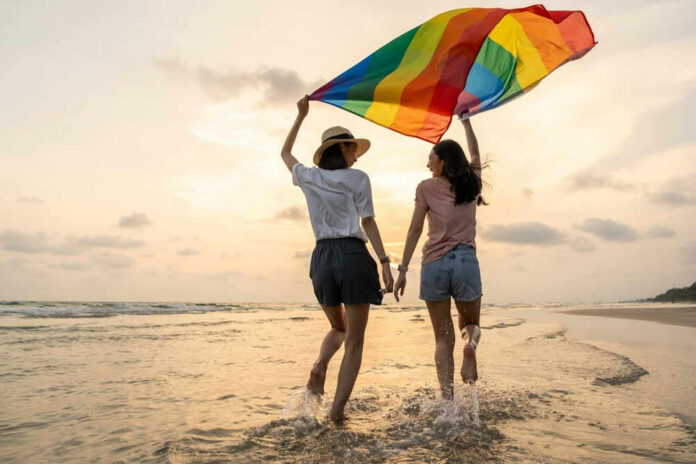 lgbtid2451404507jpg Two people with rainbow flag on beach at sunset.