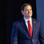 Rubio’s Oversized Shoes – A Trump Loyalty Test? Man in suit and red tie on stage