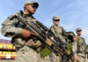 Soldiers in uniform holding weapons outdoors on sunny day