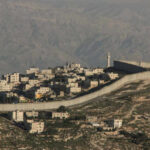 West Bank Erupts: Settler Attacks Ignite Tensions A view of a residential area bordered by a separation barrier in a mountainous region