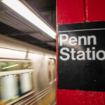 Sign for Penn Station at a subway platform with a moving train in the background