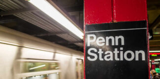 Sign for Penn Station at a subway platform with a moving train in the background
