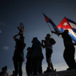 Silhouetted figures holding a trophy and Cuban flags during a celebration