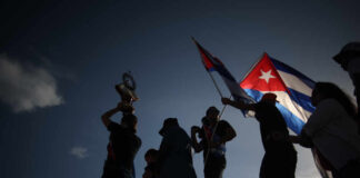 Silhouetted figures holding a trophy and Cuban flags during a celebration