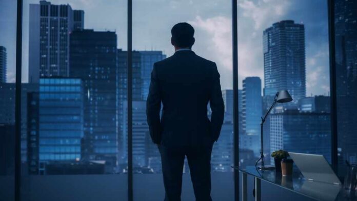 shutterstock_2093720923.jpg A man in a suit standing in an office looking out at a city skyline