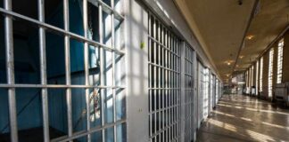 Interior view of a prison corridor with jail cells and sunlight streaming through windows