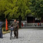 Two men in traditional attire with bicycles in a park setting