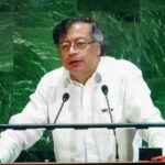 A speaker in a white shirt addressing an audience at a podium