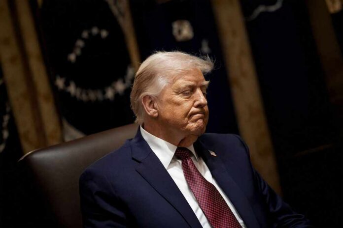 A political figure sitting with a serious expression in a formal setting