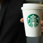 Starbucks Billionaire Bolts After Tax Slam Person holding a Starbucks coffee cup.