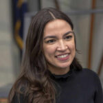 Political Fallout: AOC’s Risky Online Ally A person smiling, wearing a black shirt.