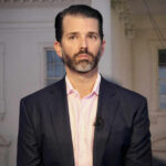 Reality TV Shake-Up: Trump Jr. as ‘Apprentice’ Host? Man in a suit standing indoors with windows background