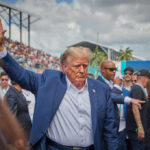 Trump Threatens to SEIZE Iran’s Nuclear Arsenal Man in blue suit waving in a crowd outdoors