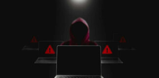 Hacker in hoodie behind laptops with warning signs