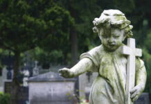 SHOCKING Daylight Shooting: 7-Month-Old Killed Weathered angel statue holding a cross in a cemetery