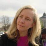 A woman with blonde hair speaking outdoors with a building in the background