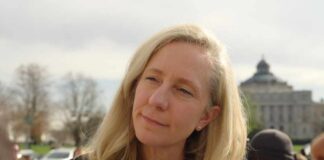 A woman with blonde hair speaking outdoors with a building in the background