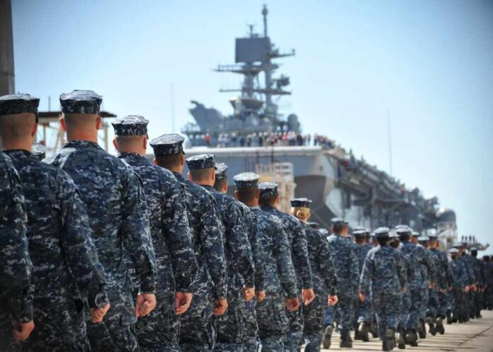 Navy personnel marching in formation towards a ship