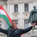 EUROPEAN IDENTITY: Hungary’s Bold New Direction Man holding a Hungarian flag while speaking at a rally in front of a statue