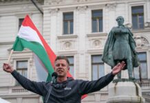 EUROPEAN IDENTITY: Hungary’s Bold New Direction Man holding a Hungarian flag while speaking at a rally in front of a statue