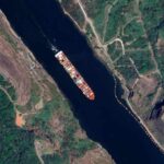 China WEAPONIZES Trade—Panama Ships Held Hostage Aerial view of a cargo ship navigating through a waterway surrounded by greenery