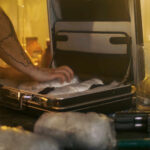 A person packing items into a suitcase in a dimly lit room