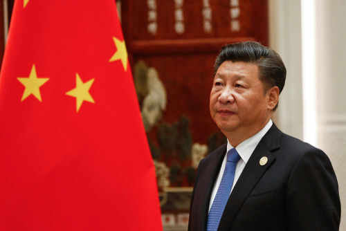 Man in suit standing beside Chinese flag indoors.