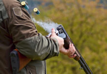 Person reloading shotgun outdoors with cartridges ejecting