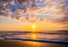 Sunset over the ocean with waves washing onto a sandy beach
