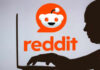 Silhouette of a person using a laptop in front of the Reddit logo