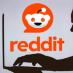 Silhouette of a person using a laptop in front of the Reddit logo