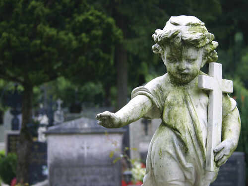 Weathered angel statue holding a cross in a cemetery