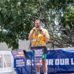 Speaker in yellow floral shirt addresses crowd at outdoor rally