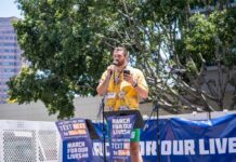Speaker in yellow floral shirt addresses crowd at outdoor rally