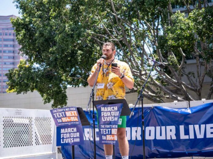 Speaker in yellow floral shirt addresses crowd at outdoor rally