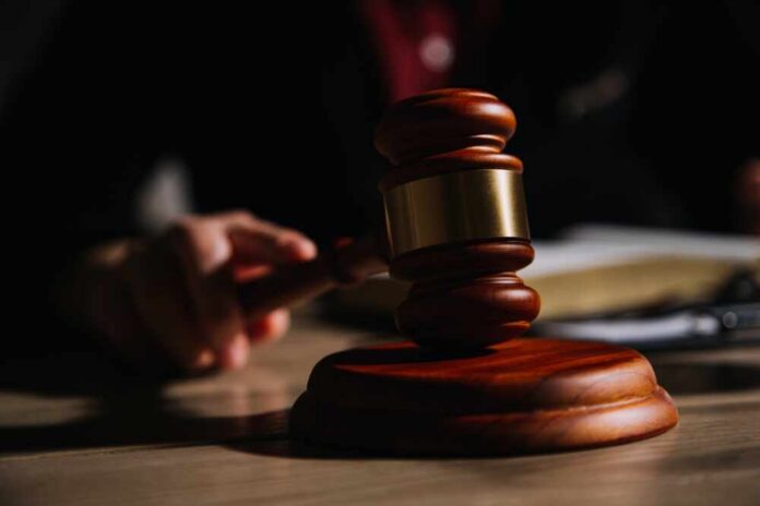 A wooden gavel resting on a table with a blurred hand in the background