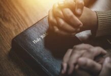 Two hands clasped in prayer over a Holy Bible