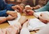 Group of hands holding each other over an open Bible