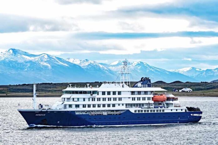shutterstock_2566845803.jpg A cruise ship sailing in front of snow-capped mountains