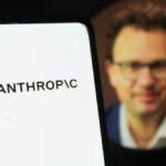 Close-up of a smartphone displaying the word 'ANTHROPIC' with a blurred portrait in the background