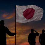 Silhouettes of soldiers saluting the Japanese flag against a sunset