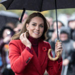 Woman in red coat holding black umbrella smiling