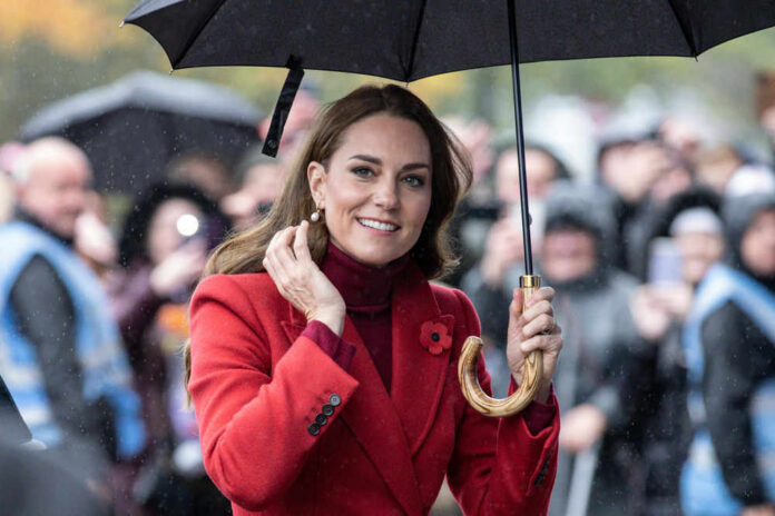 Woman in red coat holding black umbrella smiling