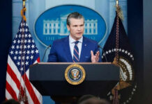 Iran Told: Locked, Loaded, Ready to Strike Man speaking at podium with flags in background