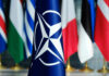 Free Riders Warned — U.S. Tab Closing NATO flag in front of various national flags
