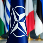 Free Riders Warned — U.S. Tab Closing NATO flag in front of various national flags